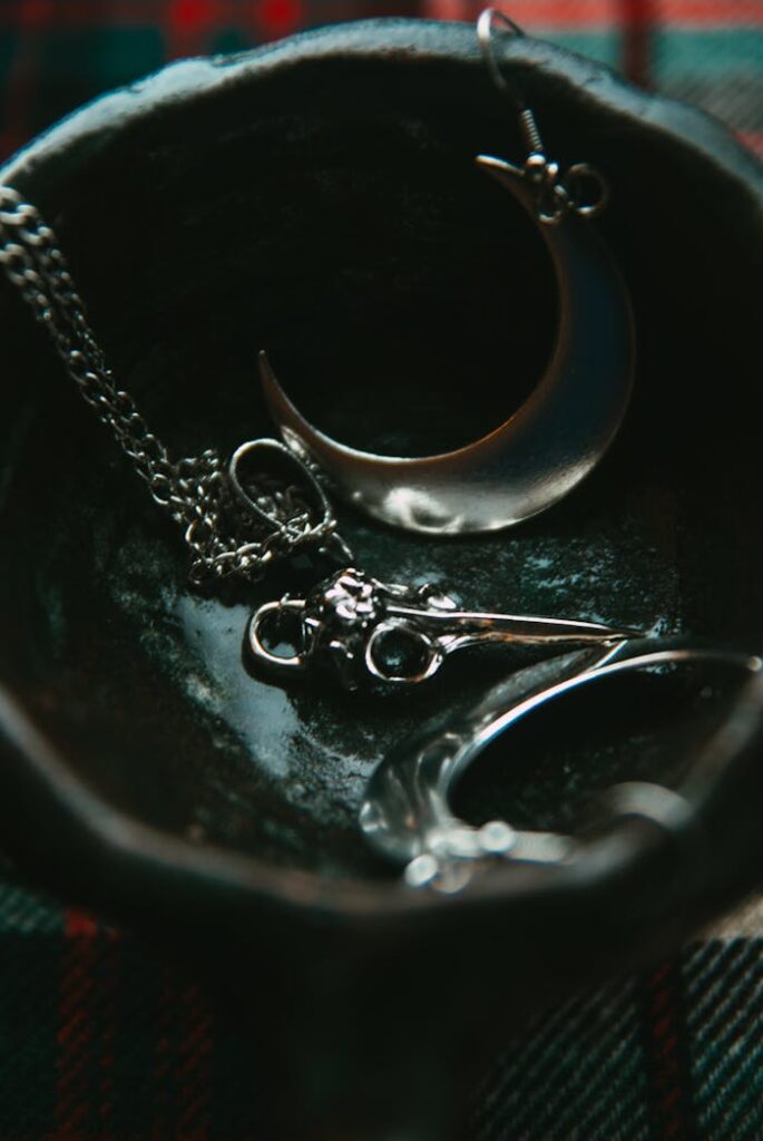 pexels photo 20002452 Close-up of silver moon and skull pendants in a dark bowl, artistic jewelry arrangement.